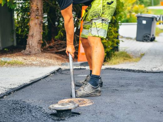Medarbetare justerar ett brunnslock i nylagd asfalt på en villauppfart