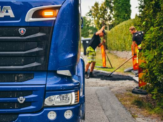 Lastbil och avspärrning på en villagata där två medarbetare jämnar ut ny asfalt
